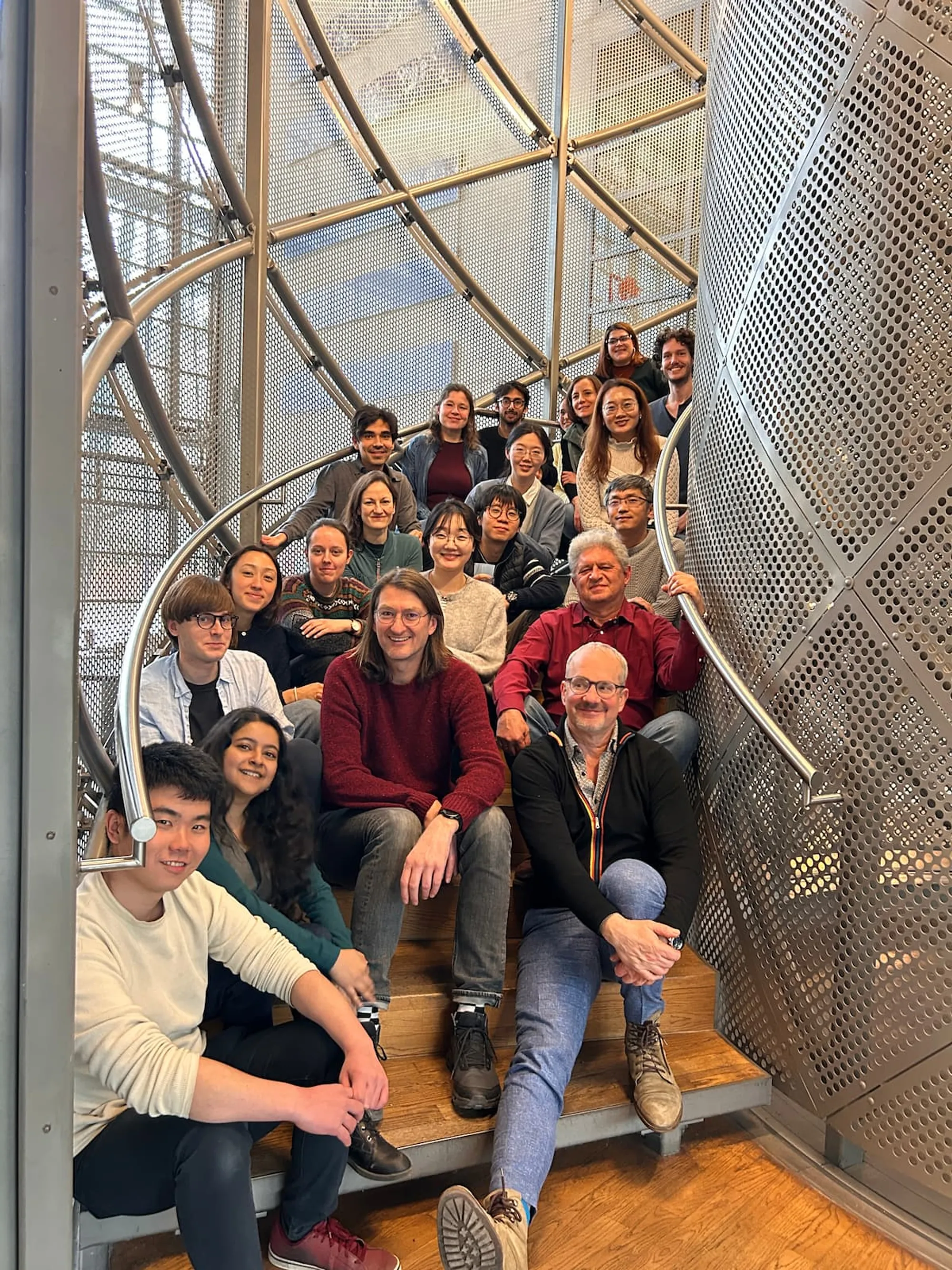 The Hyman lab members smile sitting along a spiral staircase